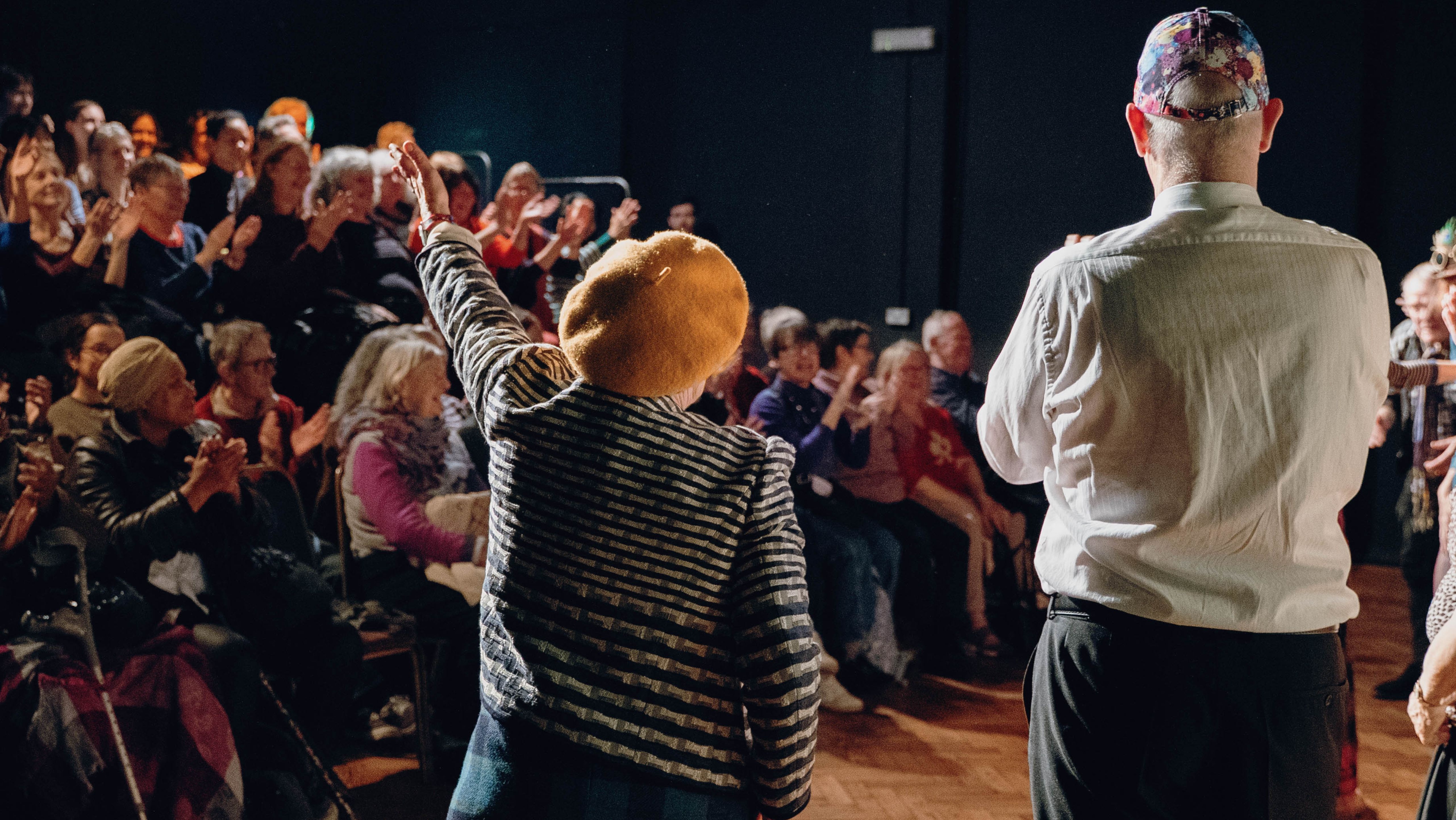 Image of a man on a woman from behind. The woman has one hand extended, as if she just blew a kiss to the audience, visible in front of her.